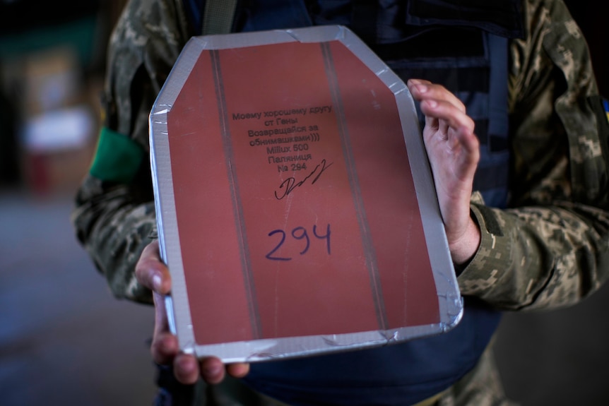 Zbliżenie dłoni żołnierza trzymającego kawałek tarczy numer 294 z ukraińskim napisem