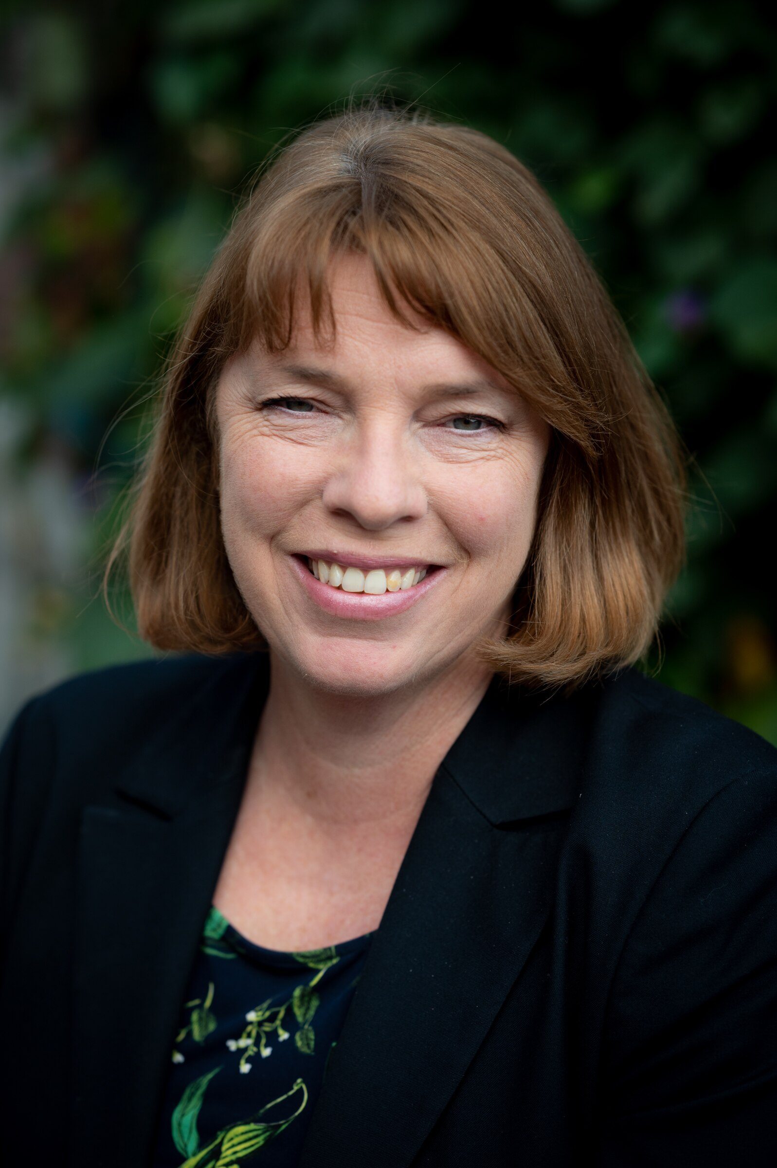 A woman with a brown bob smiling at the camera wearing a black blazer.