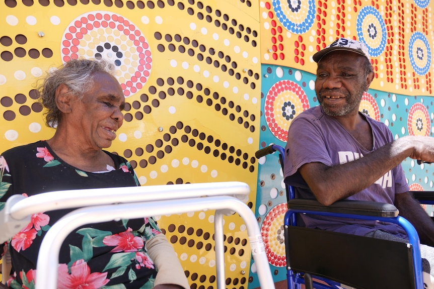 a man in a wheel chair and a woman behind a walking frame