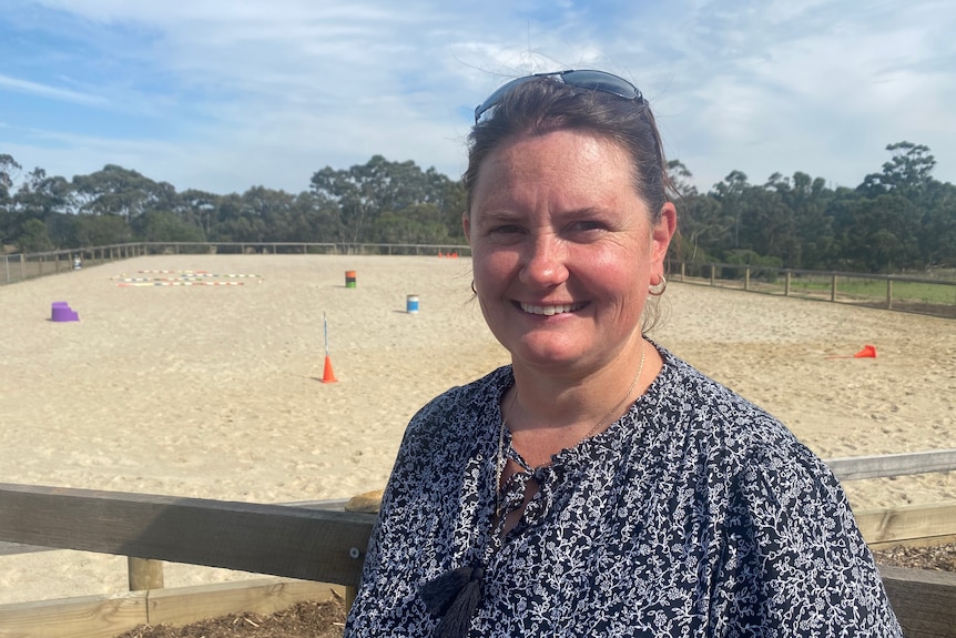 Kathryn Holden smiles at the camera, while standing in front of a sandy oval with markers.