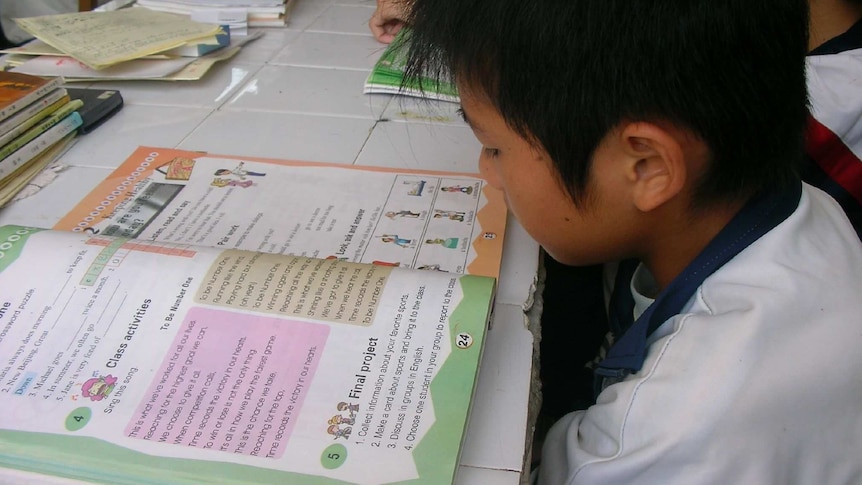 A young Chinese boy reads a textbook with English characters.
