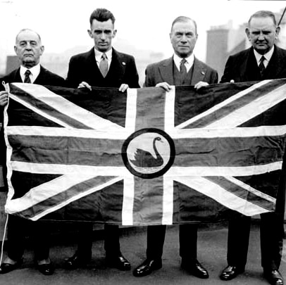 Black and white pic of four men holding the proposed new WA flag - a Union Jack with a black swan in the centre.