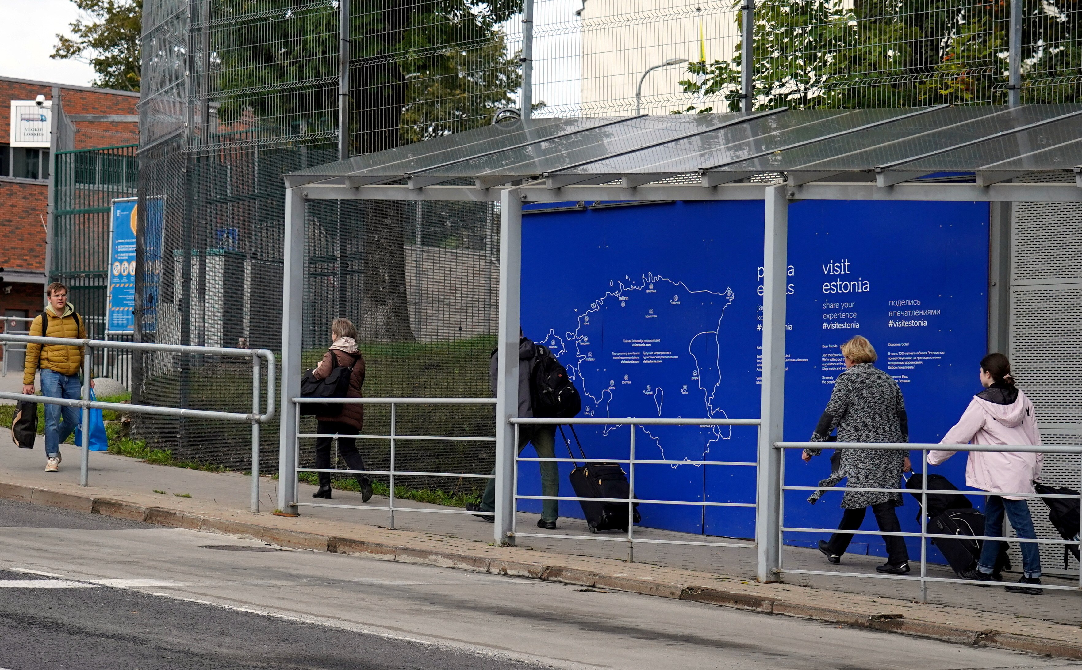People walk near the Estonian border office wheeling suitcases and trolleys. 