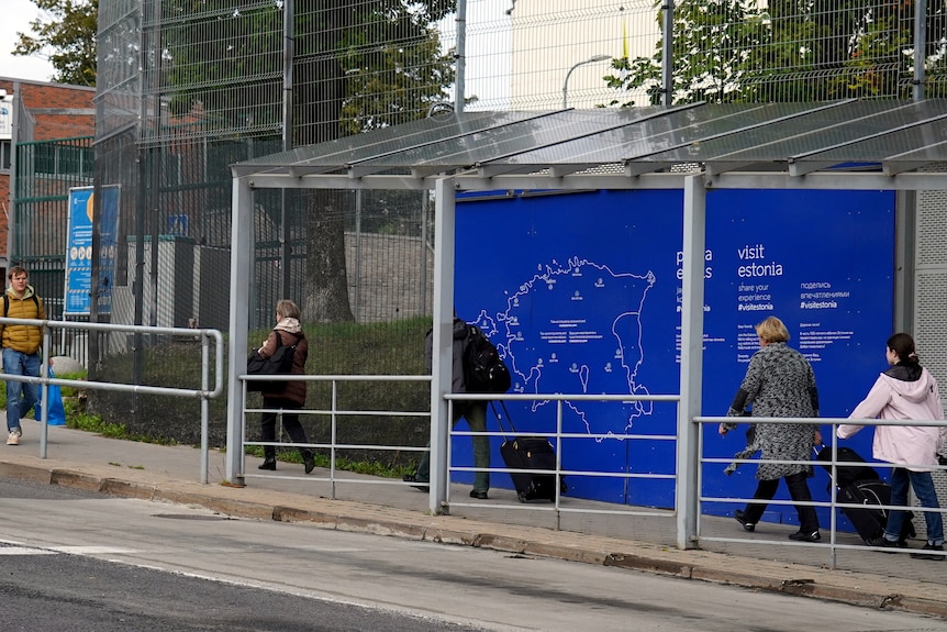 People walk near the Estonian border office wheeling suitcases and trolleys. 