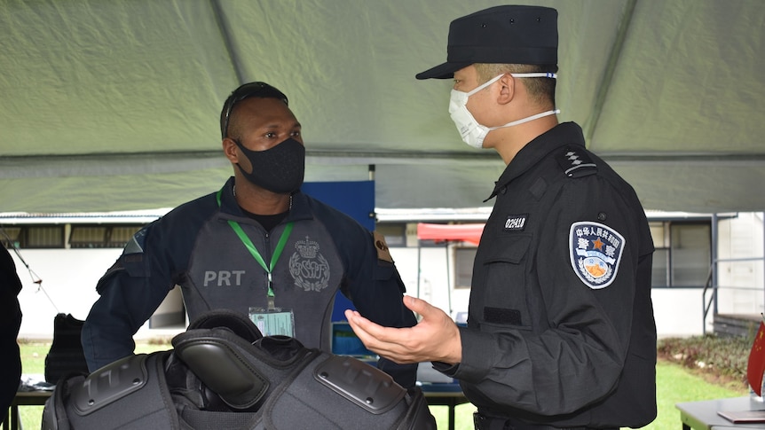 Chinese police assist PRT officer with riot vest.