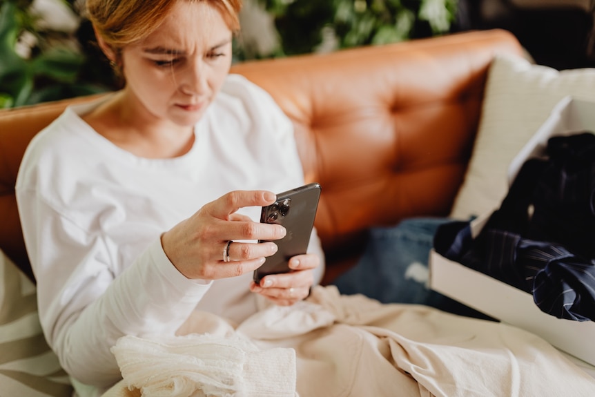 A woman with short copper hair uses her smart phone on the sofa