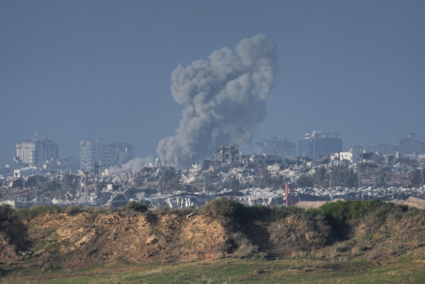 photo of smoke rising from the gaza strip behind a mound of dirt.