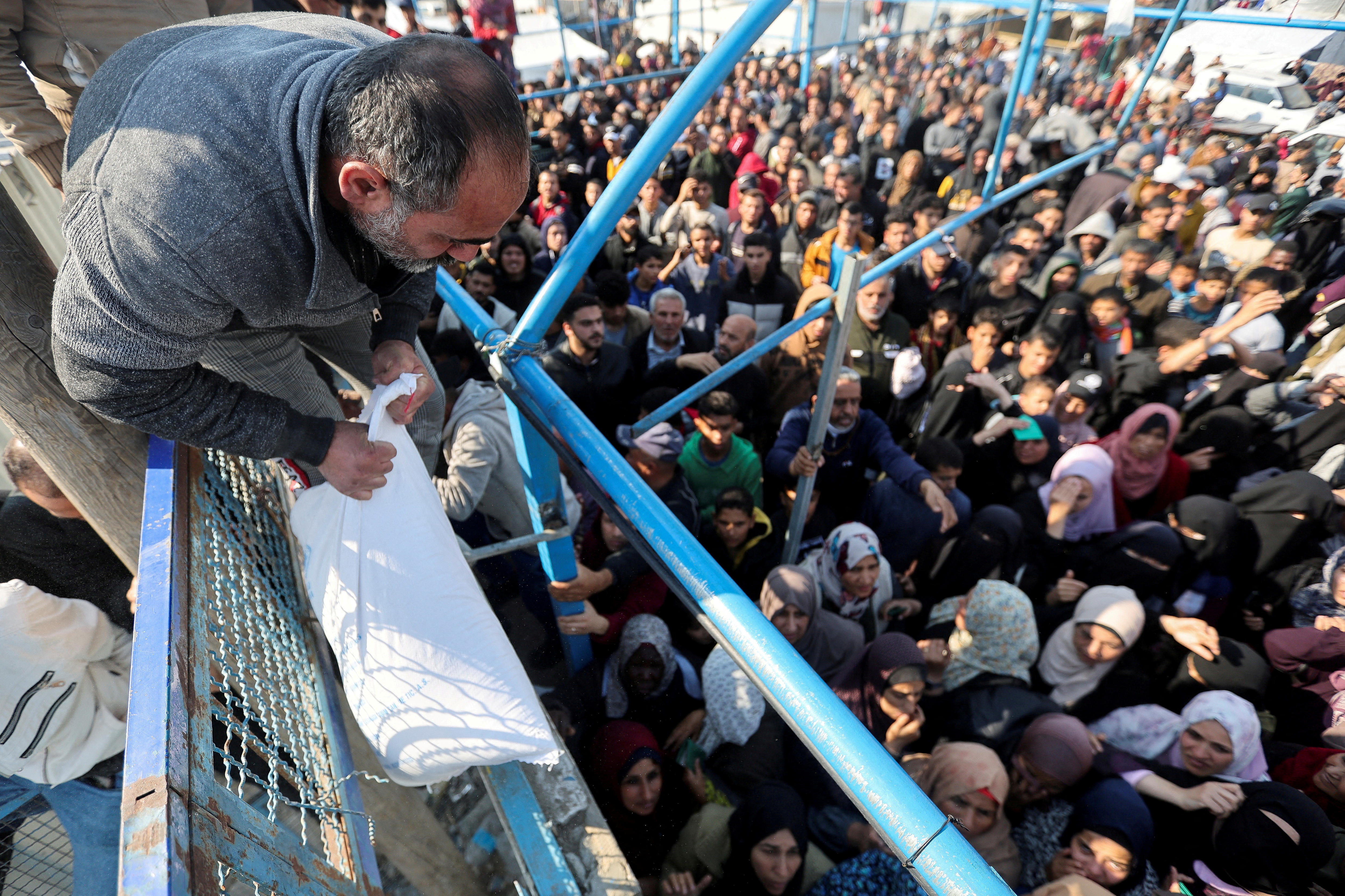 A man hands out a flour bag to a crowd of people in Khan Younis