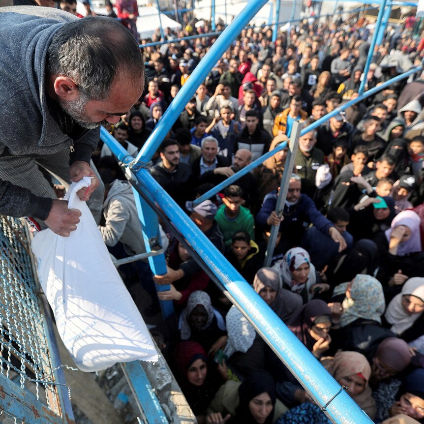 A man hands out a flour bag to a crowd of people in Khan Younis