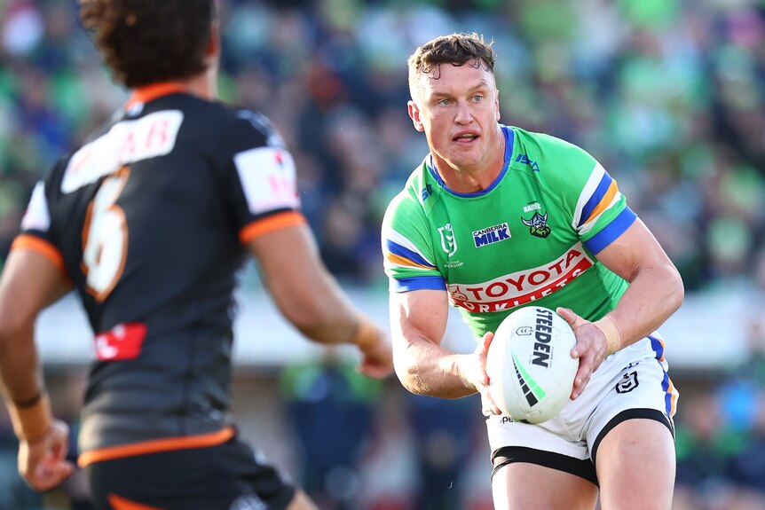 A Canberra Raiders NRL player holds the ball in two hands in a match against Wests Tigers.