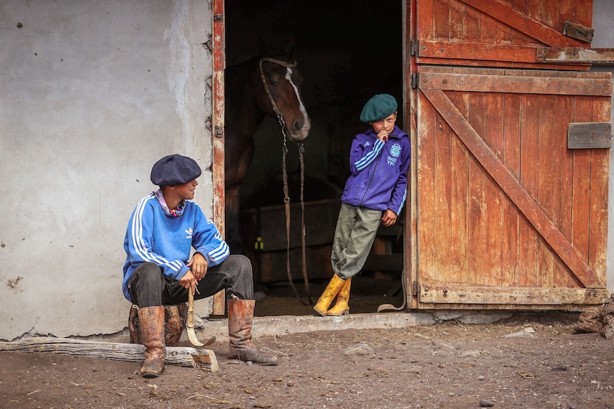 Two young boys in the doorway of a horse stable in Argentina.