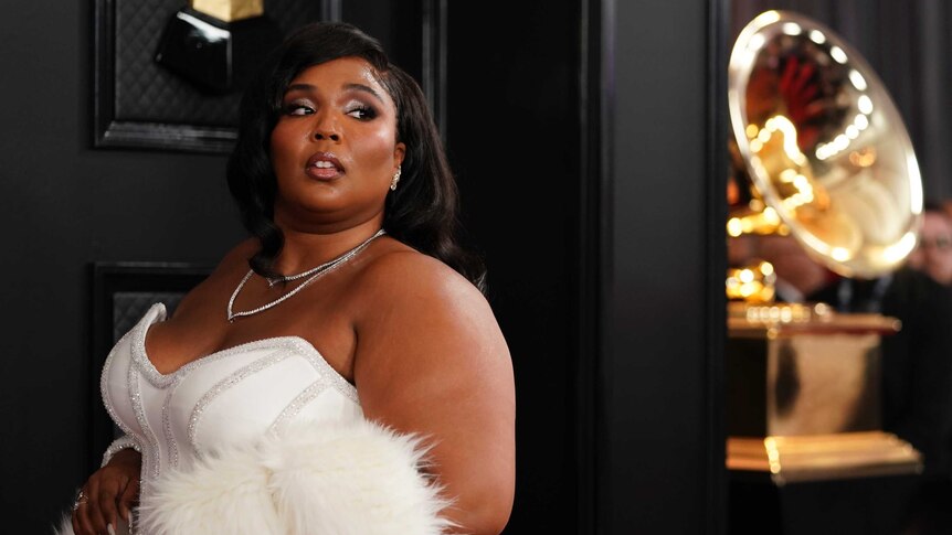 Pop star Lizzo poses on the red carpet at the Grammys wearing a white gown with a fluffy shawl.