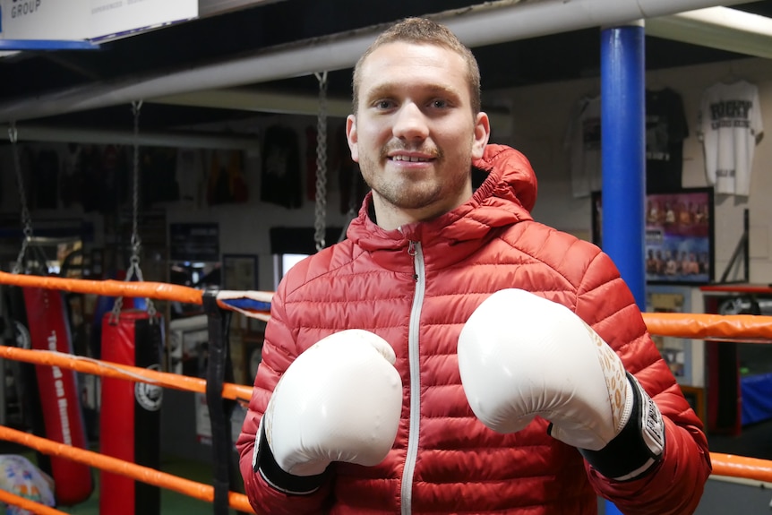 A man smiling at the camera with boxing gloves on. 