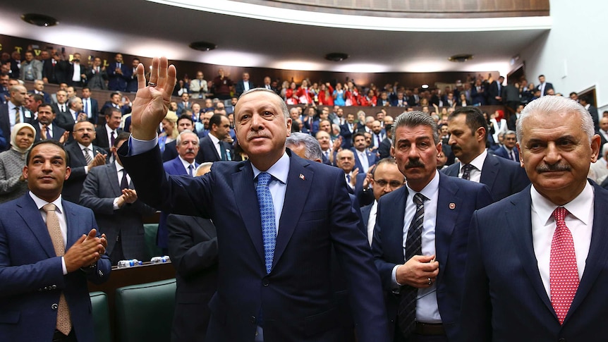 Turkey's President Recep Tayyip Erdogan waves to a crowd of politicians at a meeting.