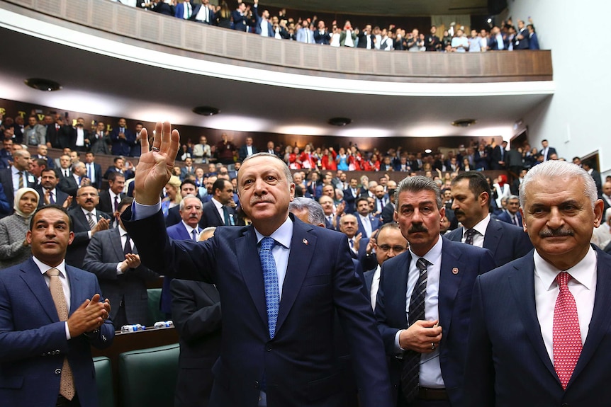 Turkey's President Recep Tayyip Erdogan waves to a crowd of politicians at a meeting.