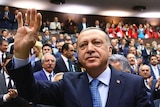 Turkey's President Recep Tayyip Erdogan waves to a crowd of politicians at a meeting.