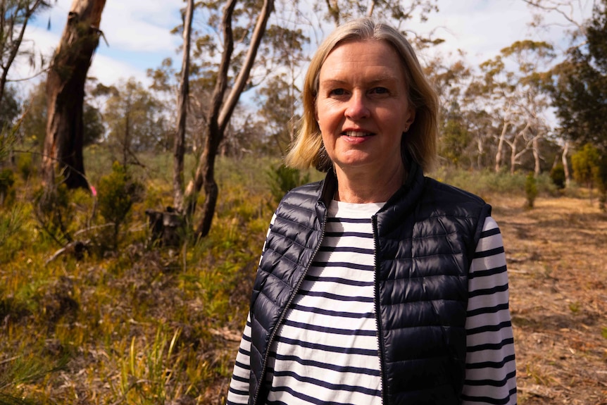 A middle-aged woman with neck-length hair stands in the bush.