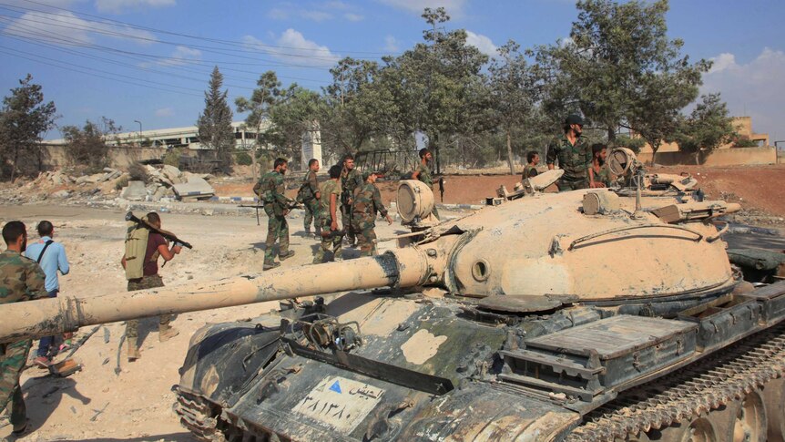 Forces loyal to Syria's President Bashar al-Assad walk past a tank at a military complex