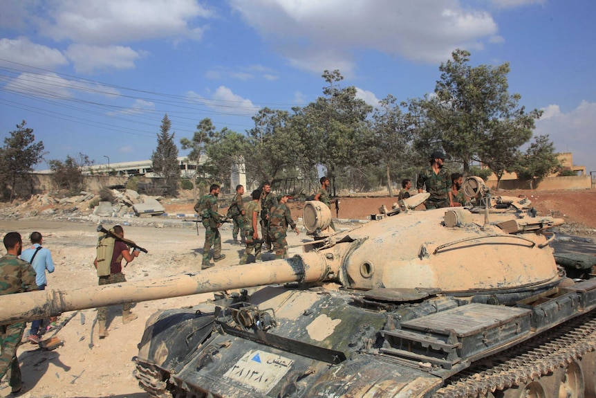 Forces loyal to Syria's President Bashar al-Assad walk past a tank at a military complex