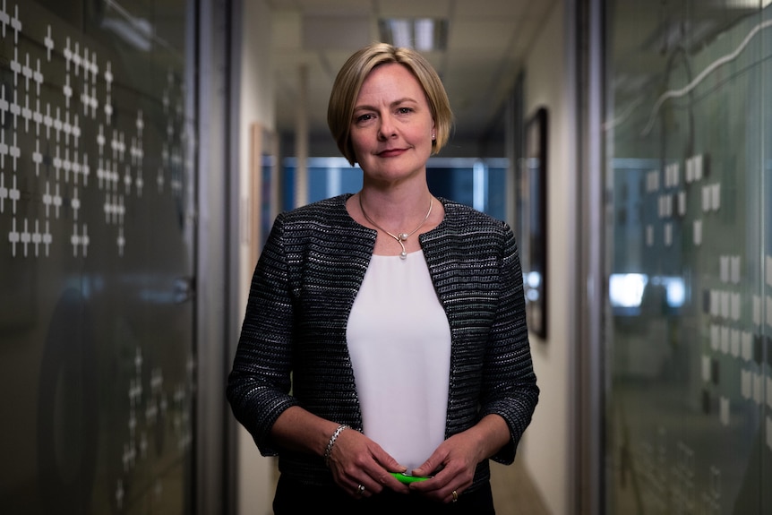 A woman with short blonde hair standing in an office hallway holding a green pen.