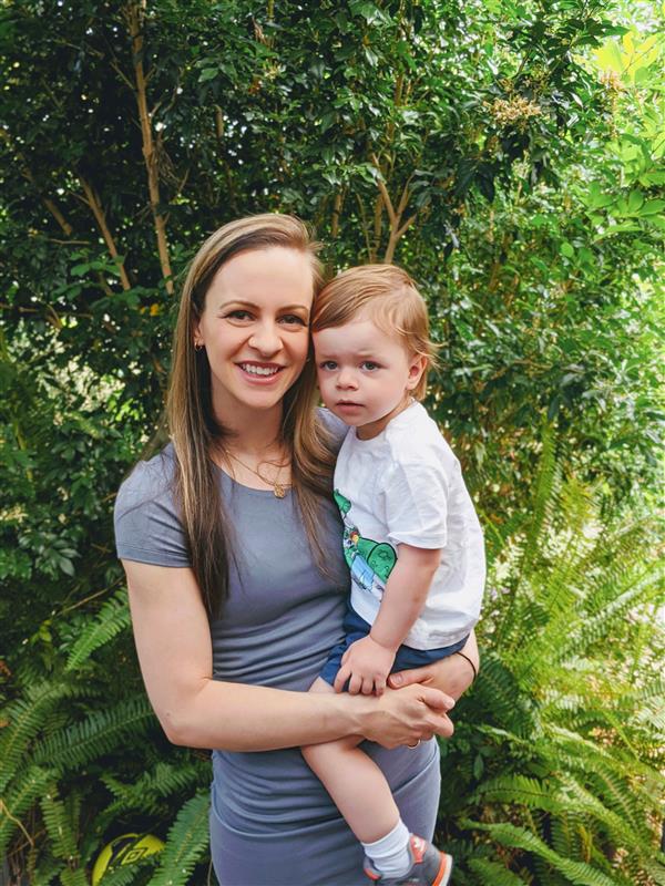 A woman stands in her backyard with a young boy on her him. She's smiling.