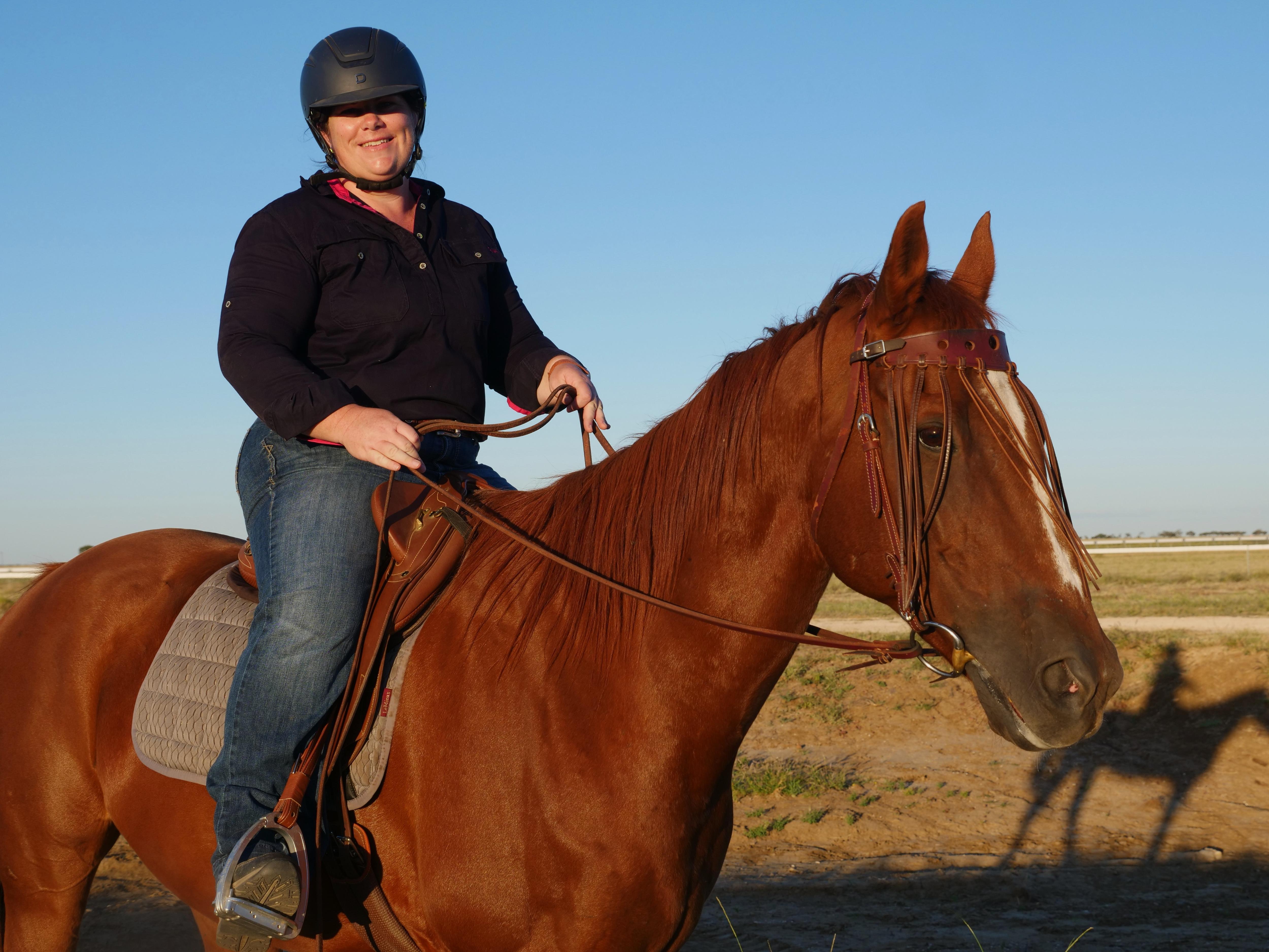 Kim Lawrence riding her horse holding the reins smiling at the camera. 