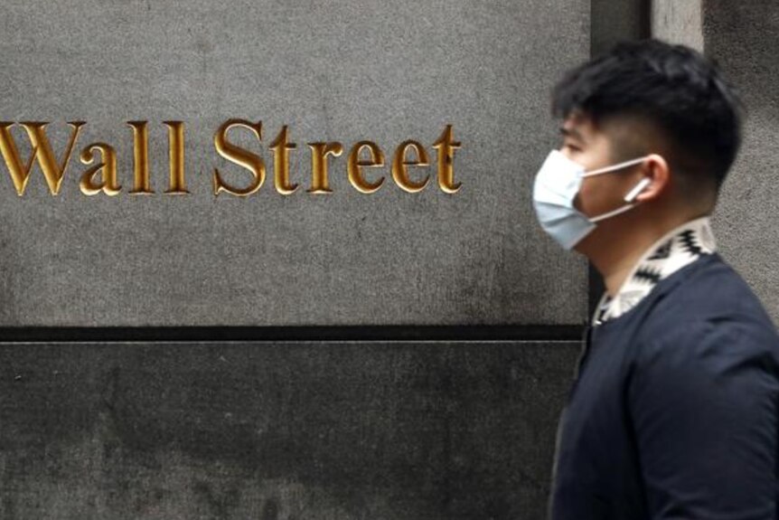 A man in wearing a surgical mask walks along Wall Street.
