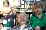 Three children smile while sitting together at a park.