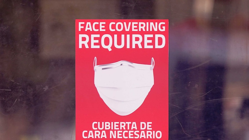 A mask required sign is displayed on the entrance to a business