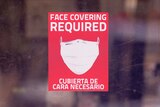 A mask required sign is displayed on the entrance to a business