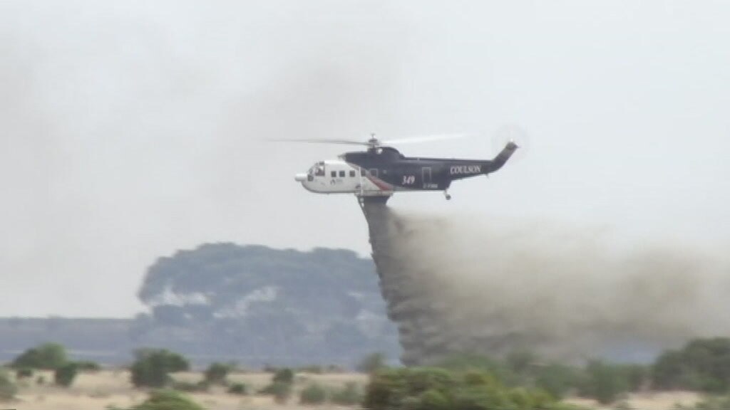 A water bombing aircraft drops liquid on a fire.