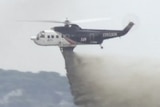 A water bombing aircraft drops liquid on a fire.