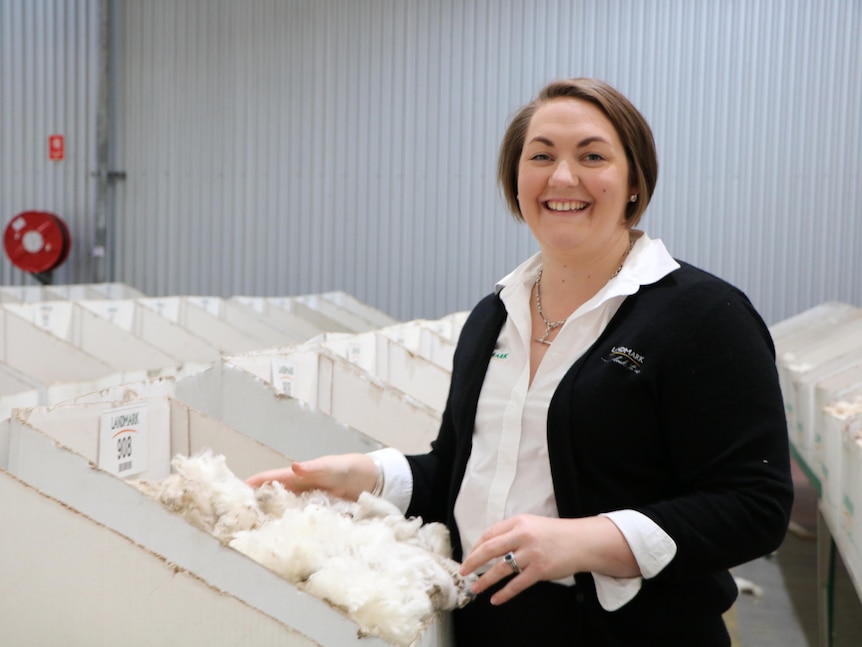 A woman smiling  and holding wool in boxes in a shed at the wool auction