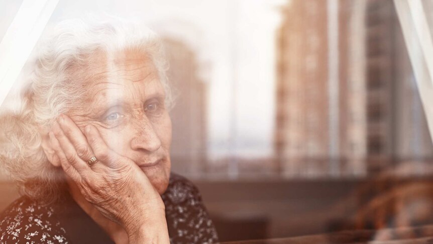 Elderly woman sitting alone and looking sadly outside the window.