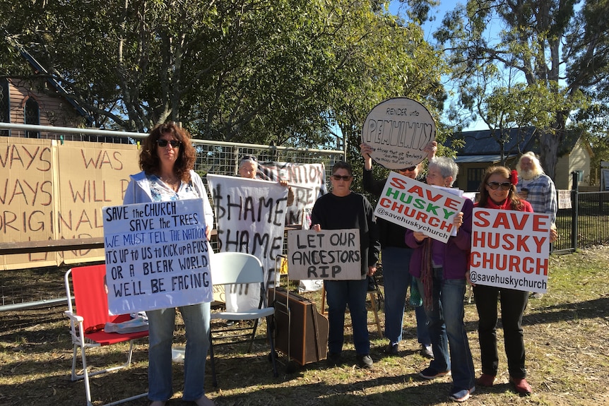 Six people hold signs such as 'Save Husky church'