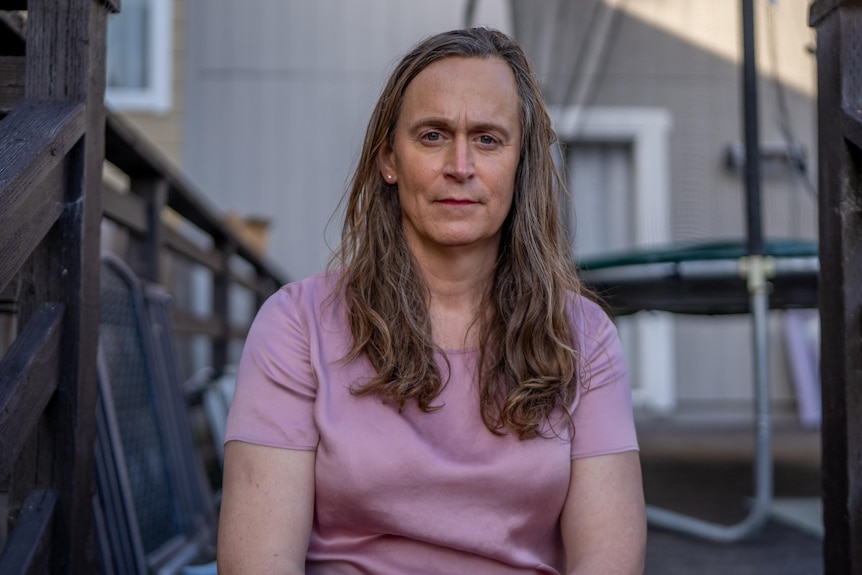 A woman with long hair sits on a staircase outdoors