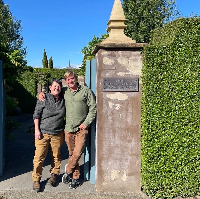 On a clear day, you view Annie Smithers and Paul Bangay smiling at the camera standing in between an ornate stone gate.