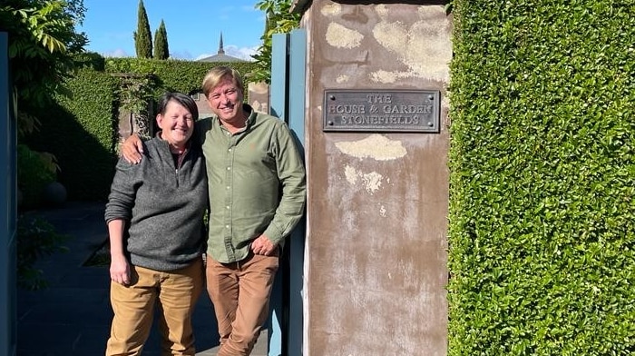On a clear day, you view Annie Smithers and Paul Bangay smiling at the camera standing in between an ornate stone gate.