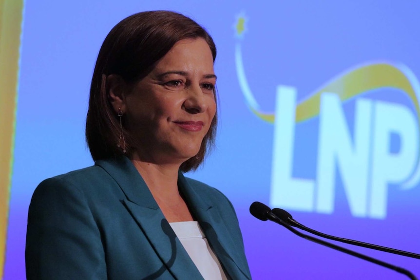 A woman in a blue blazer smiles at a microphone with "LNP" sign behind her.