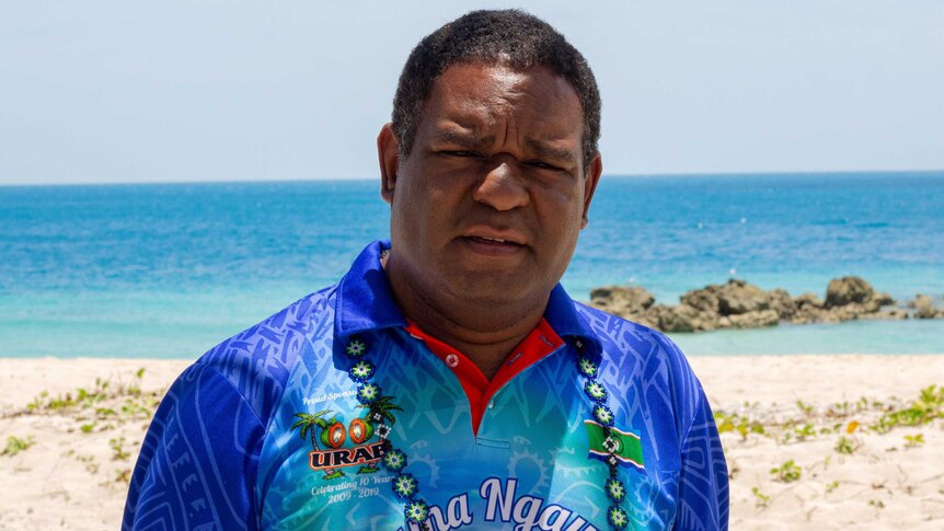 A man in a bright shirt looking at the camera, standing on the beach.