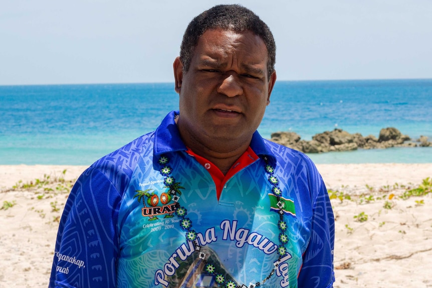 A man in a bright shirt looking at the camera, standing on the beach.