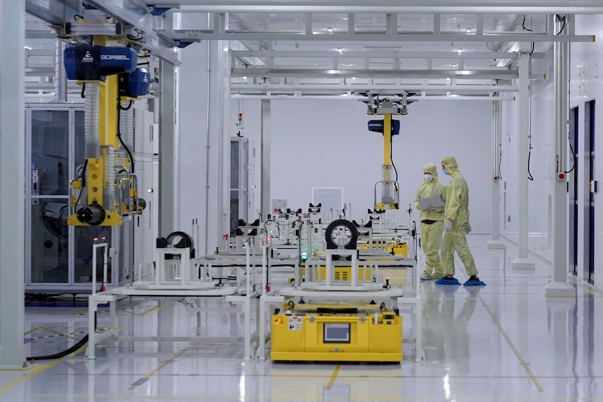 Employees in yellow outfit work in a machine lab. 