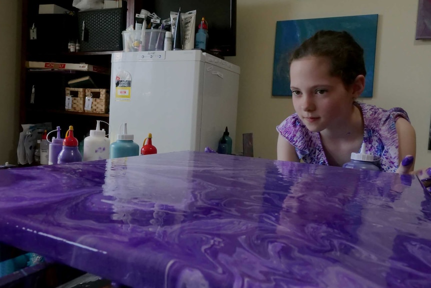 Young girl looking over the top of a canvas still wet with bright purple paint