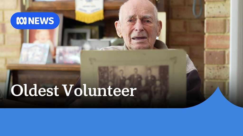 Oldest Volunteer: An elderly man holds up a sepia framed photograph.