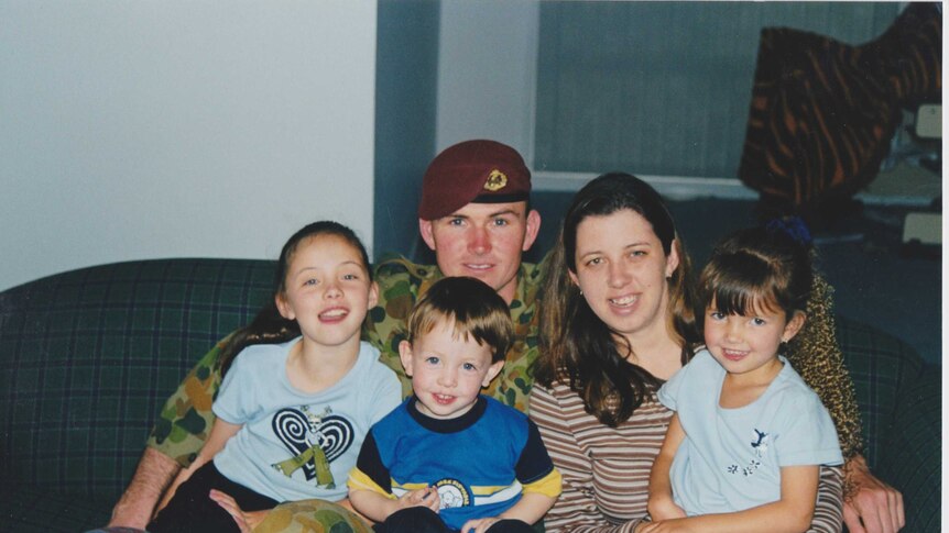 A family of five sit on the couch. Father wears an Army uniform