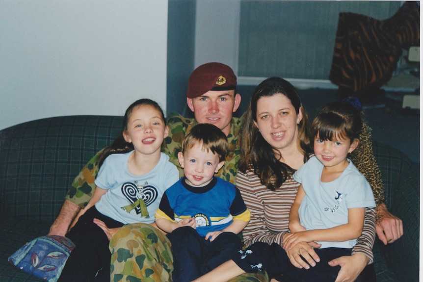 A family of five sit on the couch. Father wears an Army uniform