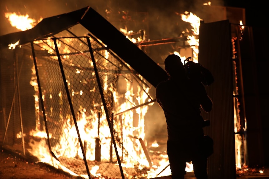 Cameraman films flames burning down building and wire fence.