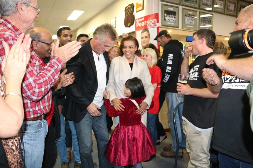 Anne Aly hugs a child as she is surrounded by clapping people.