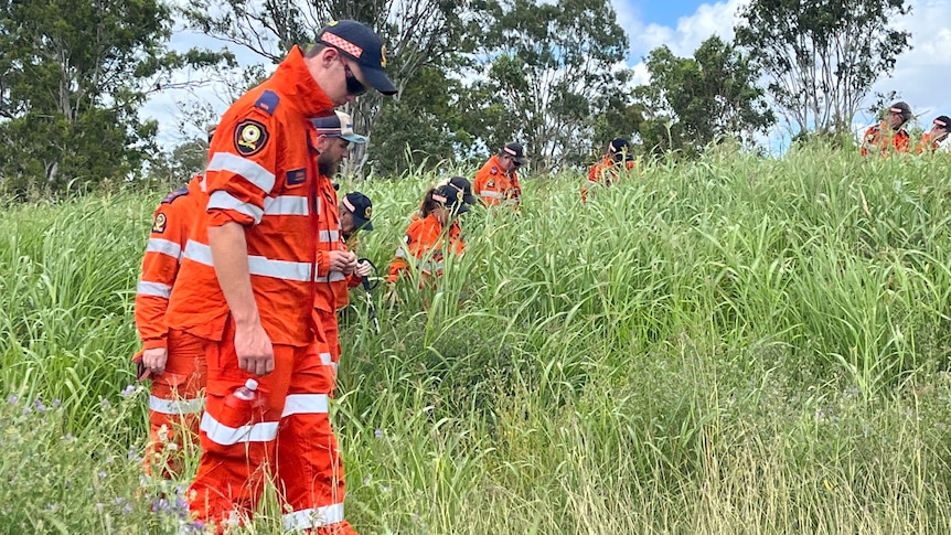 A line of people in orange uniforms looking down as they walk through high grass