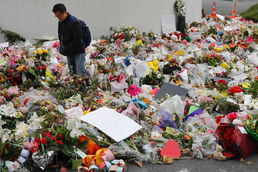 A man in a black jacket and jeans walks through a large pile of flowers.